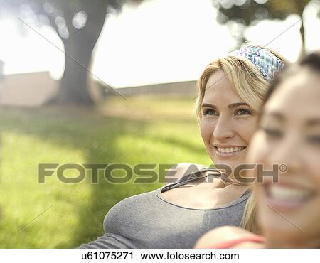 Stock Image - Close up of two young women enjoying sunshine in park. Fotosearch