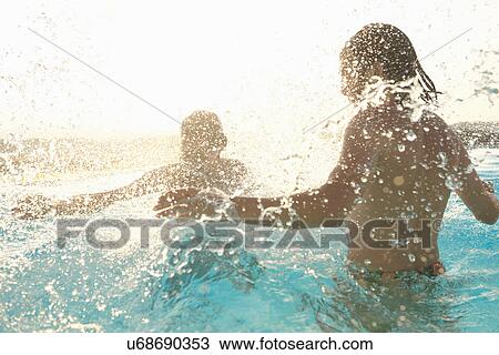 Stock Image - Couple having fun, splashing around in outdoor swimming pool. Fotosearch