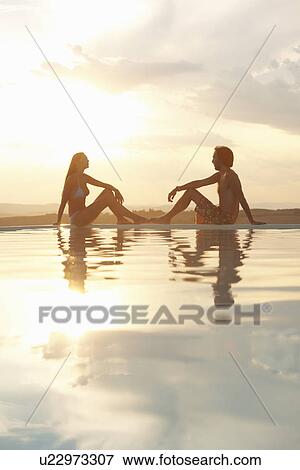 Couple sitting on infinity poolside in sunlight View Large Photo Image Stock Photo - Couple sitting on infinity poolside in sunlight. Fotosearch