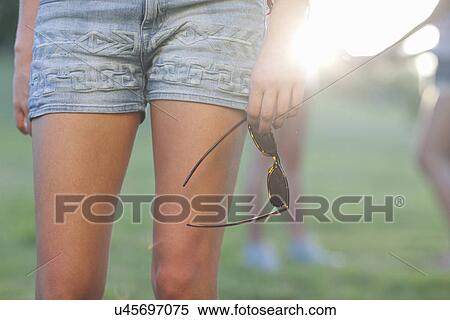 Stock Photography - Cropped image of young woman in shorts holding sunglasses. Fotosearch
