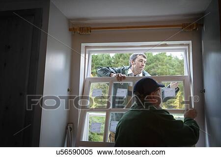 Stock Photography - Father and son builders installing new window in house. Fotosearch