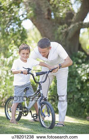 Father guiding son to cycle View Large Photo Image Stock Photo - Father guiding son to cycle. Fotosearch