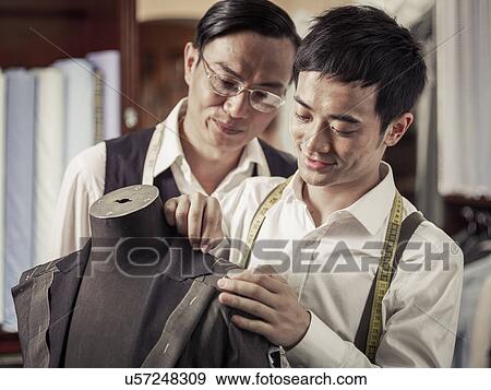 Stock Photo - Father monitoring son in family tailoring business. Fotosearch