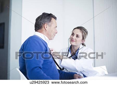 Stock Image - Female doctor holding stethoscope to patients chest. Fotosearch