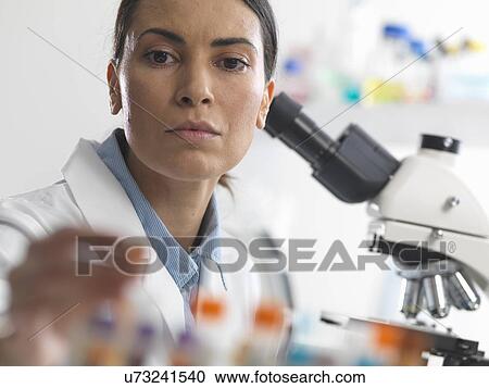 Stock Image - Female scientist about to view a blood sample under a microscope. Fotosearch