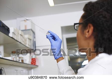 Stock Image - Female scientist looking at microscopic slide. Fotosearch