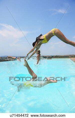 Stock Image - Four people jumping into swimming pool. Fotosearch