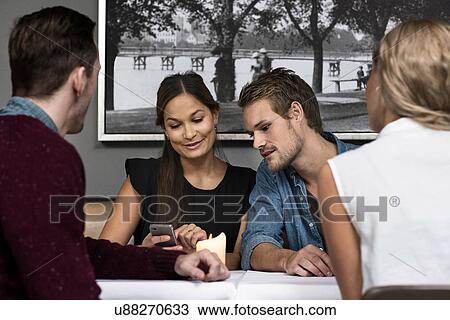 Four young adult friends sitting in cafe looking at cellphone View Large Photo Image Stock Image - Four young adult friends sitting in cafe looking at cellphone. Fotosearch