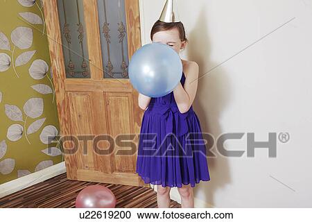 Stock Image - Girl blowing up blue balloon. Fotosearch