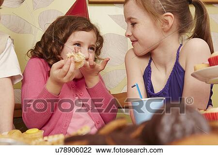Stock Image - Girl eating party food with friend. Fotosearch