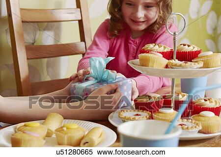 Stock Photography - Girl receiving birthday present with cakes on cakestand. Fotosearch