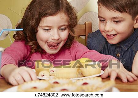 Stock Image - Girl staring at plate full of cakes, licking lips. Fotosearch