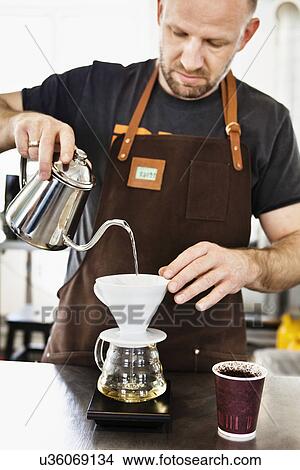 Picture - Male barista pouring boiling water into coffee filter. Fotosearch