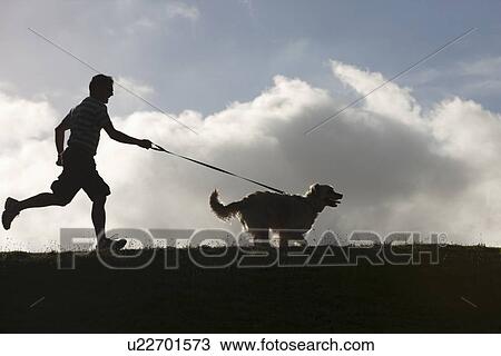 Stock Image - Man running with dog on lead. Fotosearch