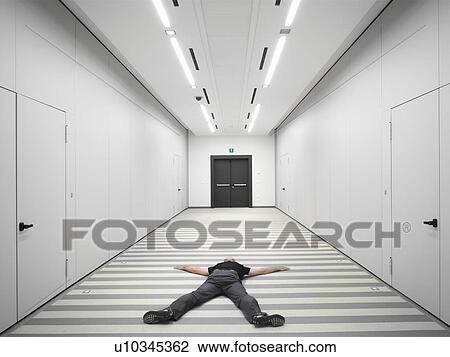 Stock Image - Man wearing black, lying on floor in white corridor. Fotosearch