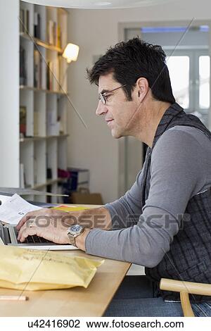 Stock Image - Mature businessman using laptop at home. Fotosearch