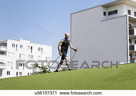 Mature male exercising with walking poles in park View Large Photo Image Stock Image - Mature male exercising with walking poles in park. Fotosearch