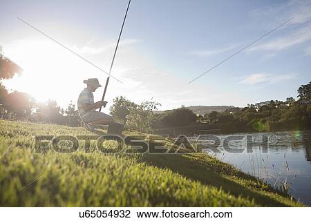 Stock Image - Mature man fishing on peaceful riverbank. Fotosearch