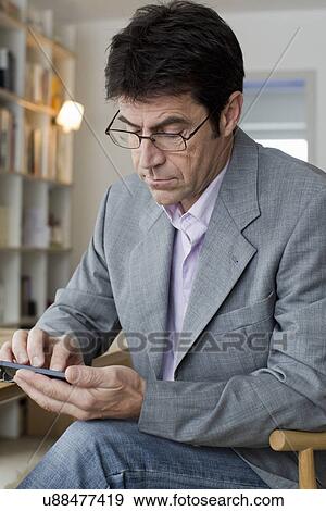 Mature man working at home texting on mobile phone View Large Photo Image Stock Photo - Mature man working at home texting on mobile phone. Fotosearch