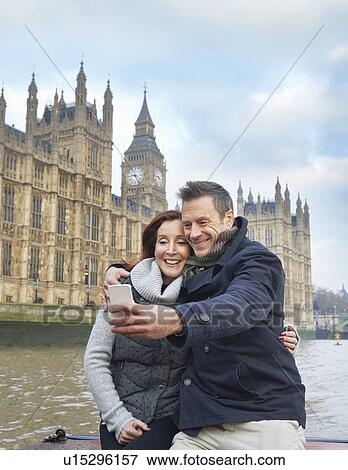Stock Photo - Mature tourist couple photographing selves and Houses of Parliament, London, UK. Fotosearch