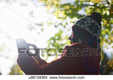Picture - Mature woman photographing with camera phone in autumn park. Fotosearch
