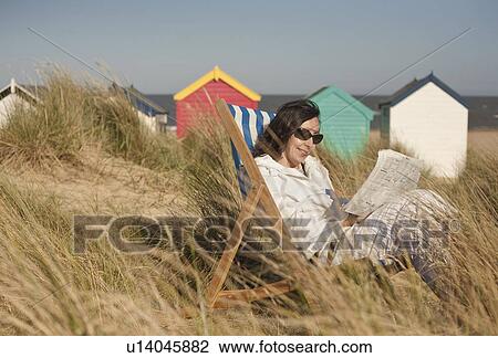 Stock Image - Mature woman relaxing on deckchair, Southwold, Suffolk, UK. Fotosearch
