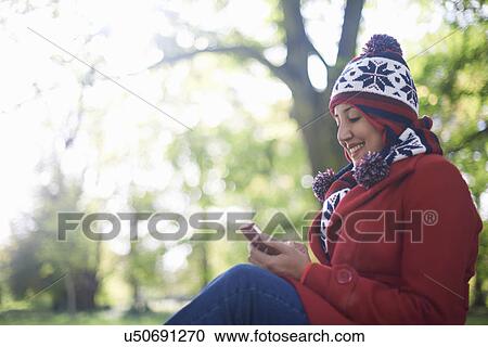 Stock Image - Mature woman texting on cellphone in autumn park. Fotosearch