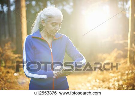 Stock Photograph - Mature woman wearing tracksuit top checking the time. Fotosearch