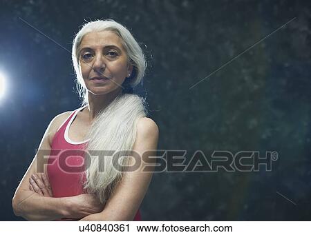 Stock Image - Mature woman with long grey hair wearing pink vest. Fotosearch