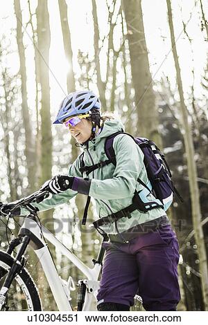 Stock Image - Mid adult female mountain biking pushing bike through forest. Fotosearch