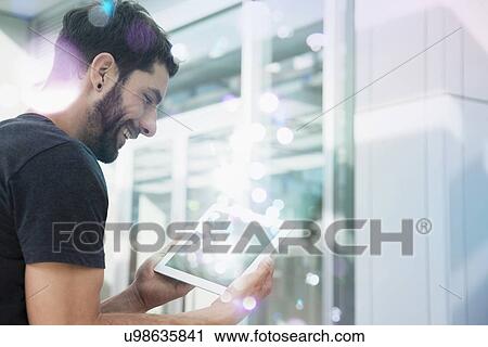 Stock Image - Mid adult man looking at lights coming from digital tablet. Fotosearch