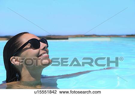 Stock Image - Mid adult woman wearing sunglasses relaxing in pool. Fotosearch