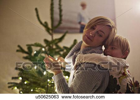 Stock Image - Mother and son hugging next to christmas tree. Fotosearch