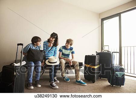 Stock Image - Mother and two sons with wheeled cases at airport. Fotosearch