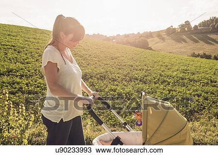 Stock Image - Mother strolling in countryside pushing baby pram. Fotosearch