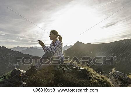 Stock Photo - Portrait of a mid adult woman backpacker using smartphone, Achensee, Tyrol, Austria. Fotosearch
