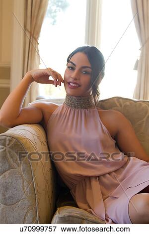 Stock Photo - Portrait of attractive young woman on sofa in evening dress. Fotosearch