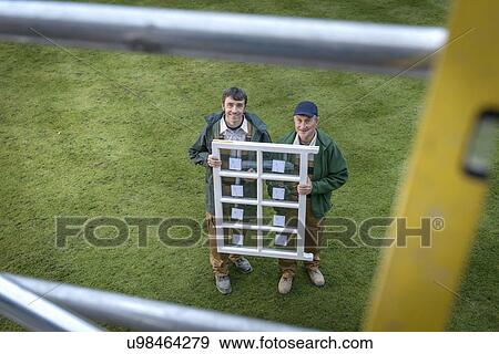 Stock Photo - Portrait of father and son builders holding new window, high angle view. Fotosearch