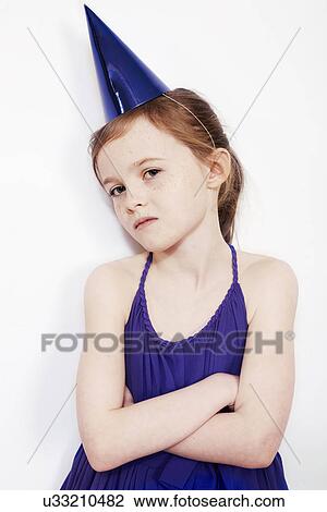 Stock Image - Portrait of girl wearing party hat with arms folded. Fotosearch