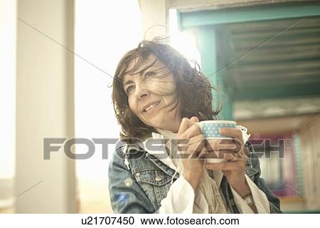 Stock Image - Portrait of mature woman with cup of coffee, Southwold, Suffolk, UK. Fotosearch