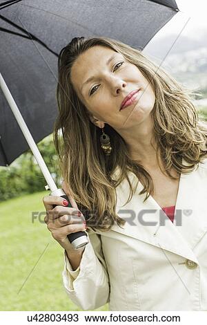 Stock Image - Portrait of mid adult woman holding up umbrella. Fotosearch