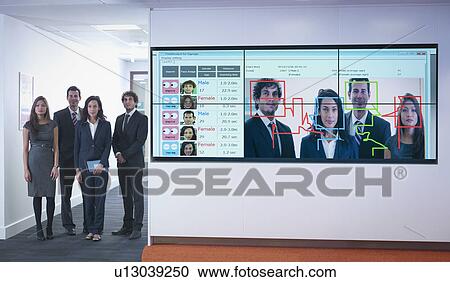Stock Image - Portrait of office workers standing next to face recognition software system. Fotosearch