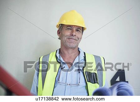 Stock Image - Portrait of senior male surveyor holding blueprints. Fotosearch