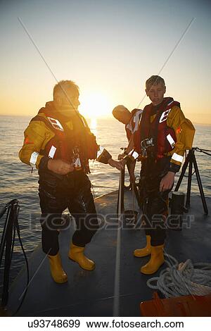 Stock Photo - Portrait of three men holding lifeboat railing at sea. Fotosearch