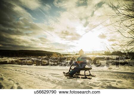 Stock Image - Portrait of young boy sitting on toboggan on rural road. Fotosearch
