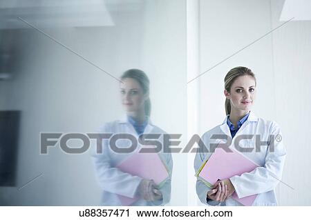 Stock Image - Portrait of young female doctor holding notes. Fotosearch