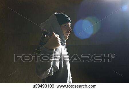 Stock Image - Portrait of young man holding skateboard. Fotosearch
