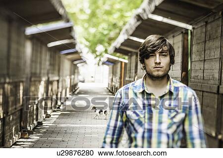 Stock Image - Portrait of young man standing between wooden buildings. Fotosearch