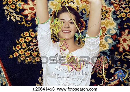 Stock Image - Portrait of young woman and streamers lying on patterned rug. Fotosearch