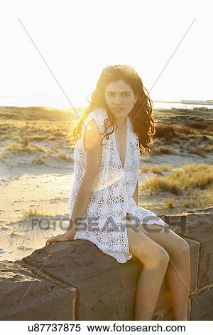 Stock Photography - Portrait of young woman sitting on wall. Fotosearch